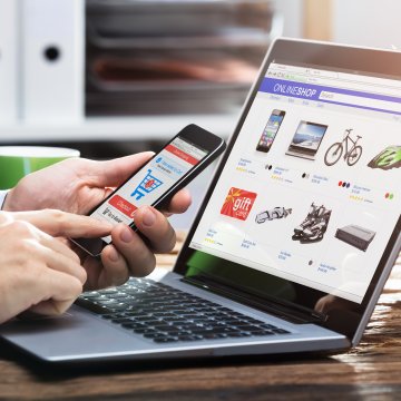 man on smartphone in front of laptop ecommerce shopping online
